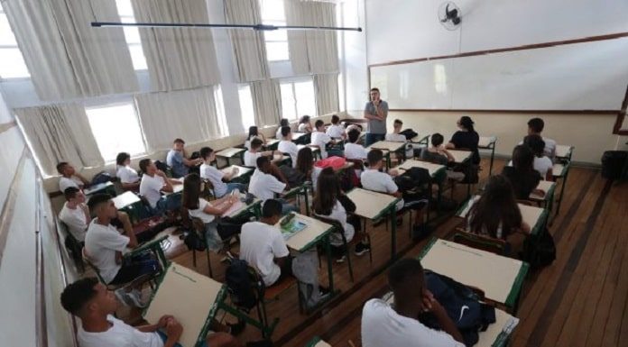 sala de aula cheia, com estudantes sentados nas carteiras e professor à frente em pé