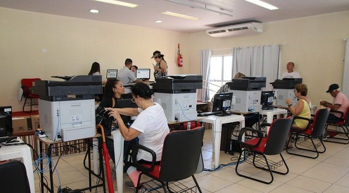 computadores instalados sobre mesas lado a lado com pessoas sentadas em cadeiras em ambos os lados