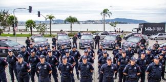 agentes da guarda alinhados em sentido com viaturas ao fundo estacionadas ordenadas em volta, na frente da prefeitura