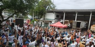 grande grupo de funcionários da comcap uniformizados com os braços para cima reunidos no pátio da companhia e gazebo do sindicato à frente com homem ao microfone