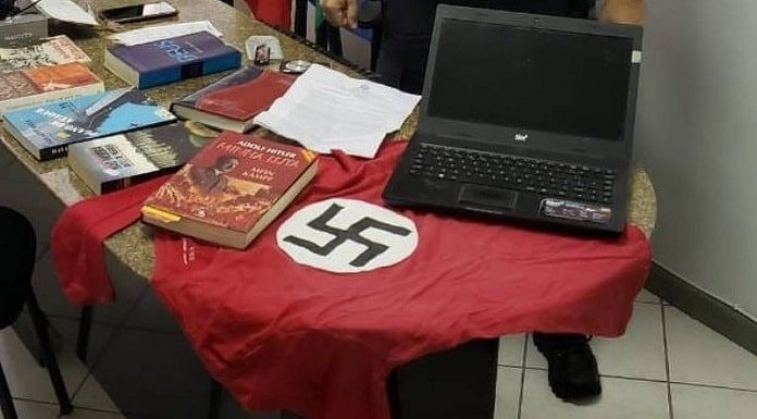 sobre uma mesa de mármore estão diversos livros do nazismo, camiseta com suástica e notebook