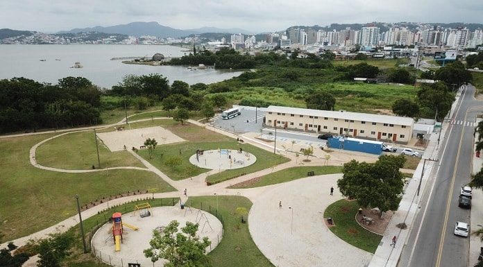 foto aérea do parque, com pista de caminhada, grande gramado mar ao fundo e pequenos apartamentos ao lado