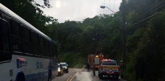 bombeiro limpando o asfalto com mangueira e marca de óleo que desce a via, ao lado de ônibus, caminhão dos bombeiros e viatura da polícia