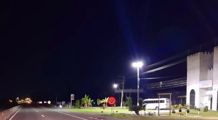 trecho da rodovia com ciclofaixa em foto noturna com alguns imóveis na beira da rodovia