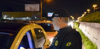 agente da prf com aparelho bafômetro na janela de um carro apontando com sinal verde na blitz em via marginal