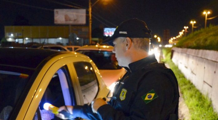 agente da prf com aparelho bafômetro na janela de um carro apontando com sinal verde na blitz em via marginal