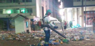 homem com uniforme da comcap e soprador limpa grande área cheia de lixo no centro