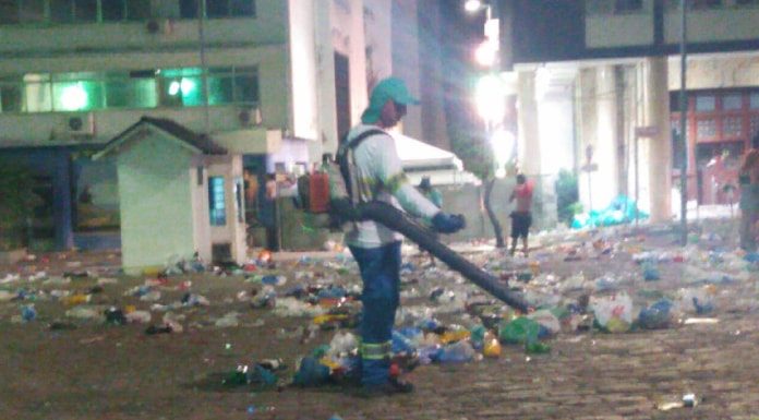 homem com uniforme da comcap e soprador limpa grande área cheia de lixo no centro