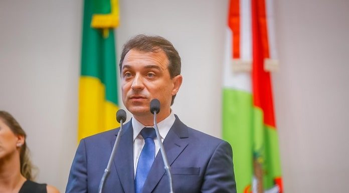 moisés na tribuna da alesc falando ao microfone com bandeira do brasil e de sc ao fundo