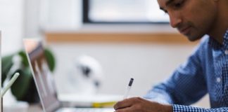 homem fazendo anotaçoes em um caderno ao lado de um notebook