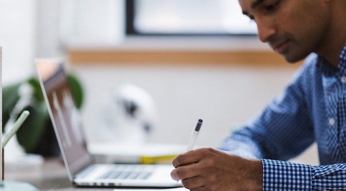 homem fazendo anotaçoes em um caderno ao lado de um notebook