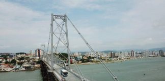 ônibus do transporte coletivo municipal de florianópolis passando pela ponte hercílio luz em foto aérea com o mar abaixo