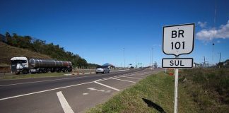 placa com inscrição br 101 sul ao lado da rodovia em dia de sol passando carros e caminhão