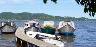 três barcos ancorados lado a lado junto ao final de um pier na lagoa e embarcação do outro lado