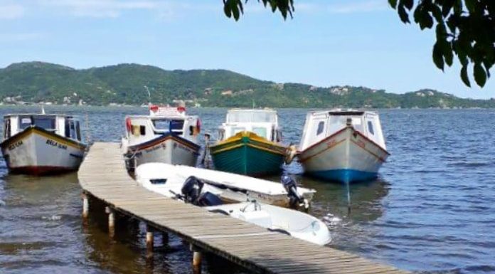 três barcos ancorados lado a lado junto ao final de um pier na lagoa e embarcação do outro lado