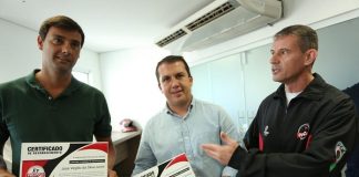 três homens posam para foto, com prefeito no meio com certificado na mão olhando para a câmera