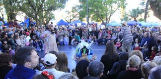 grande público reunido em volta de um pequeno palco ao centro onde há apresentação de boi de mamão