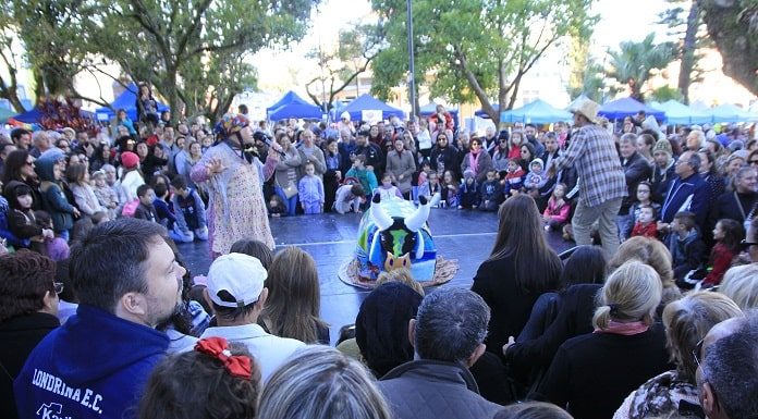 grande público reunido em volta de um pequeno palco ao centro onde há apresentação de boi de mamão