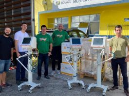 três respiradores fora das caixas com prefeito e outros quatro homens em volta posando para a câmera, ao lado de um caminhão baú aberto e em frente à secretaria de saúde