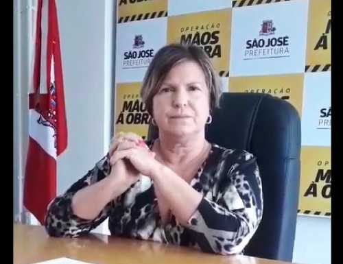 adeliana sentada atrás de uma mesa com painel ao fundo com logos da prefeitura