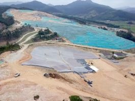 vista aérea do aterro sanitário de biguaçu, com boa parte de terra exposta, lonas por cima e máquinas circulando; montanhas ao fundo