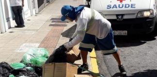 gari da comcap se baixa para pegar caixas e sacolas de lixo em calçada