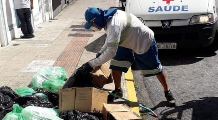 gari da comcap se baixa para pegar caixas e sacolas de lixo em calçada