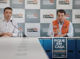 zeferino e moisés na ponta de uma mesa com cartaz à frente "fique em casa"