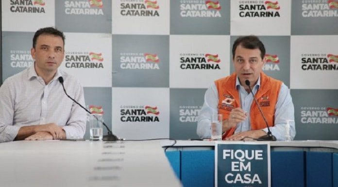 zeferino e moisés na ponta de uma mesa com cartaz à frente "fique em casa"