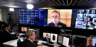 vice-presidente do senado sentado em mesa com dois monitores e na parede diversos outros monitores