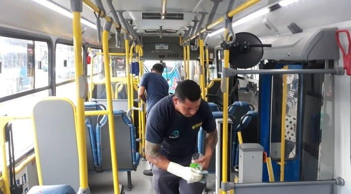 dois homens com luvas e alcool gel fazem limpeza dentro de ônibus