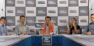 moisés e mais quatro pessoas em bancada de coletiva com painel ao fundo com logos do governo de sc