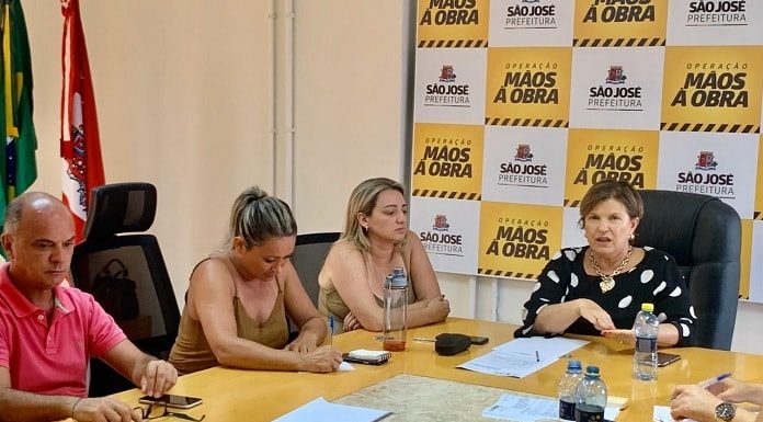 prefeita e secretárias reunidas em volta de uma mesa e painel com logos de são josé ao fundo