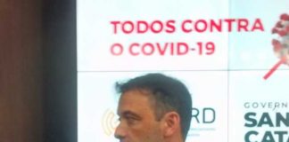 secretário dando entrevista com painel ao fundo escrito covid-19