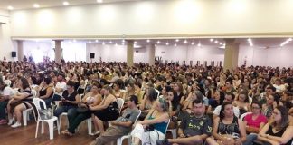 centenas de pessoas sentadas em cadeiras de plástico em grande salão