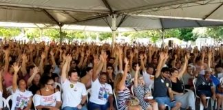 centenas de pessoas sentadas sob área coberta com os braços levantados