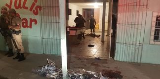 corpo no chão coberto com manta metálica em frente ao bar e alguns policiais em volta