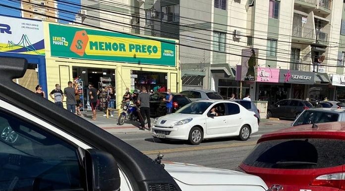 caminhonete da defesa civil e carro do procon municipal estacionados em avenida com comércios do outro lado da rua