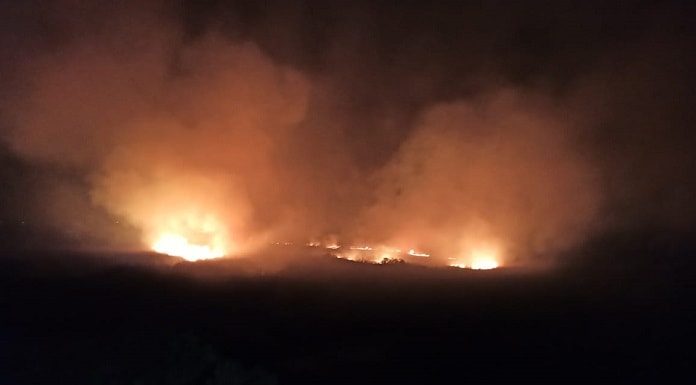 incêndio visto à distância em meio a grande área escura com muita fumaça