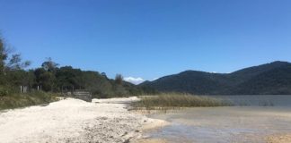 parte de areia na margem da lagoa, com a água no centro da imagem e montanhas ao fundo