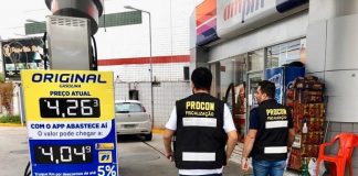 dois fiscais do procon com coletes identificativos entrando em um posto com placa de valor da gasolina de R$4,26