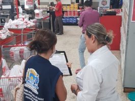 fiscal da vigilância mostra prancheta para mulher funcionária do supermercado, perto dos caixas