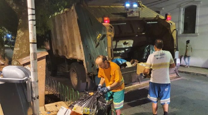 dois funcionários da comcap atrás de caminhão compactador estacionado na av. hercílio luz onde há pilha de lixo no calçadão