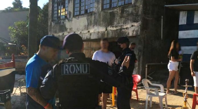 agente da guarda com inscrição ROMU nas costas fala com um homem na areia da praia e há pessoas e outros agentes em volta