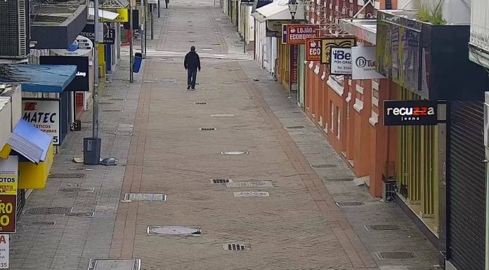 homem usando moletom e calça jeans é visto em imagem de camera de rua andando sozinho em calçadão com comércio em volta fechado no centro de florianópolis