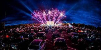 dezenas de carros estacionados em drive-in com show ao fundo