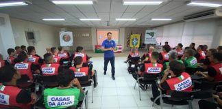 árbitro em pé dando aula em sala com outros homens usando colete da casas da água