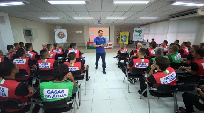 árbitro em pé dando aula em sala com outros homens usando colete da casas da água