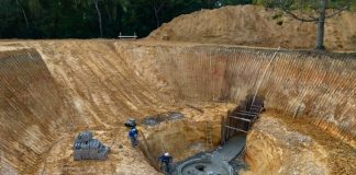 enorme buraco de obra circular escavado com mais um buraco ao centro com trabalhadores assentando tijolos em círculo