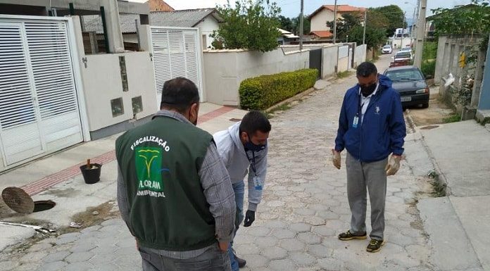 três homens usando máscaras se inclinam sobre tampa de bueiro em meio à servidão